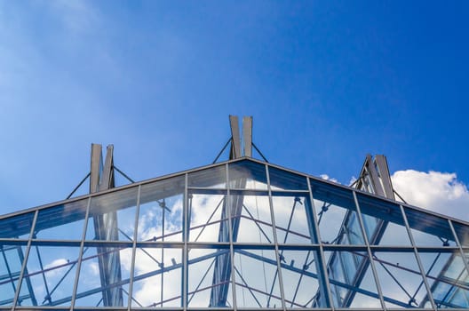 Glass roof in a steel structure against a blue sky with clouds.