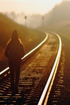 Young girl walking along railroad at sunset