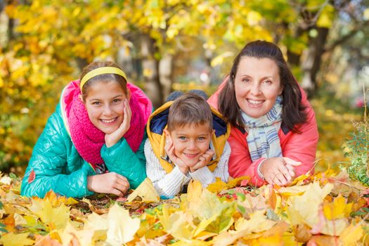 Happy family relaxing in autumn park - mother with her kids has fun in park.
