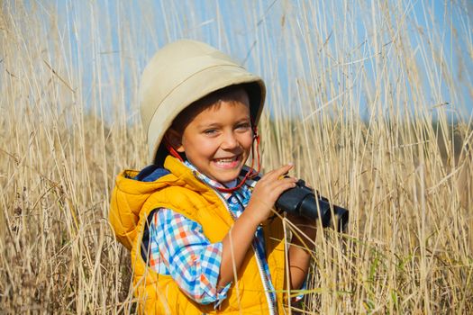 Young boy child playing pretend explorer adventure safari game outdoors with binoculars and bush hat