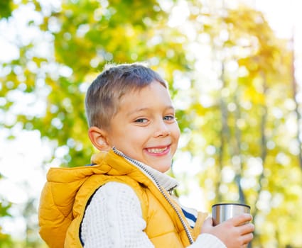 Portrait of Adorable cute boy resting and drinking tea from a thermos in the beauty autumn park 