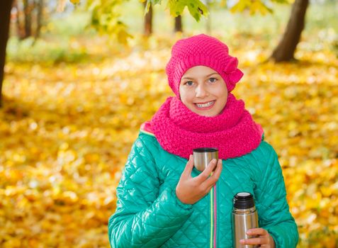 Portrait of Adorable cute girl resting and drinking tea from a thermos in the beauty autumn park 