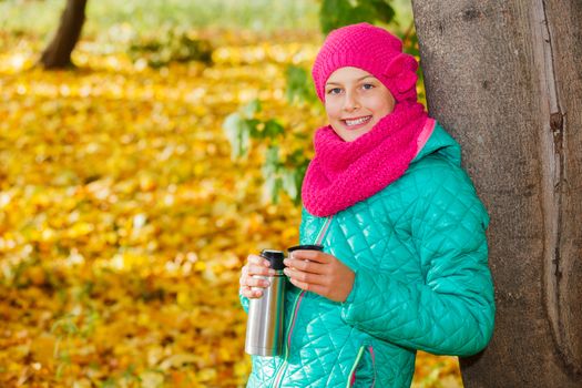Portrait of Adorable cute girl resting and drinking tea from a thermos in the beauty autumn park 