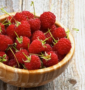 Perfect Ripe Raspberries with Stems in Wooden Bowl Cross Section on Rustic Wooden background