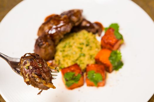 Organic meat of lamb cooked with slices of pumpkin and quinoa in oriental style on a white plate