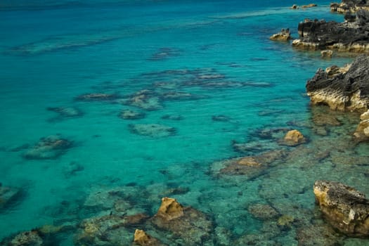 Clear, tropical sea, with underwater reef clearly visible, along with coastal rocks