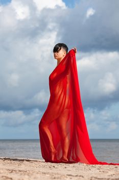 Young naked woman on a beach with red fabric