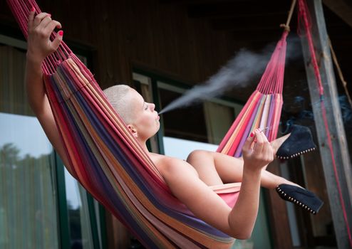 Young sensual nude woman with cigarette resting in a hammock