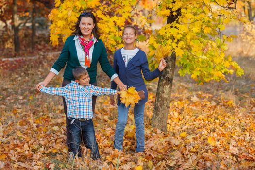 Happy family relaxing in autumn park - mother with her kids has fun in park.