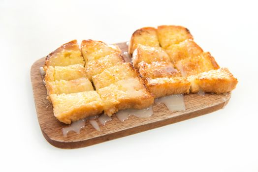 Bread toast and condensed milk on wooden plate over white background