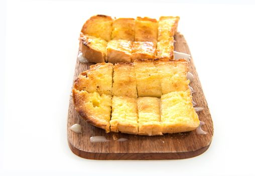 Bread toast and condensed milk on wooden plate over white background