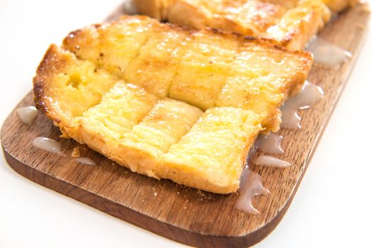 Bread toast and condensed milk on wooden plate over white background