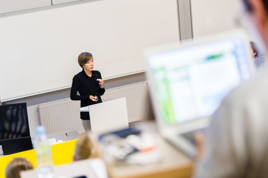 Speaker giving presentation in lecture hall at university. Participants listening to lecture and making notes.