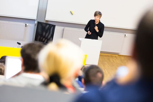 Speaker giving presentation in lecture hall at university. Participants listening to lecture and making notes.