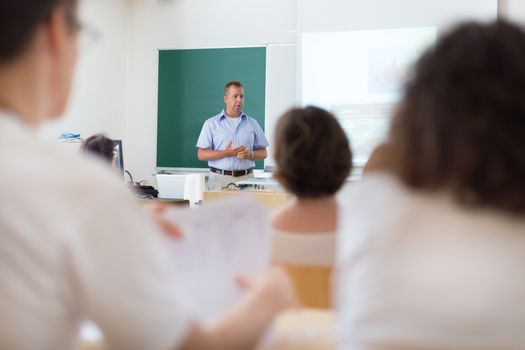 Teacher at university in front of a whiteboard screen. Students listening to lecture and making notes.