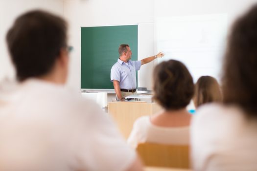 Teacher at university in front of a whiteboard screen. Students listening to lecture and making notes.