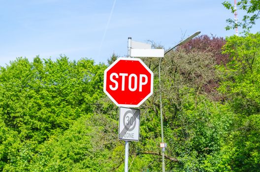 Stop sign in front of green trees and a blue sky
