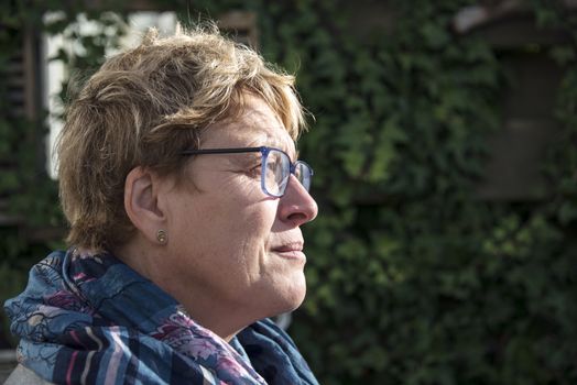 woman with golden hair and glasses thinking in the garden