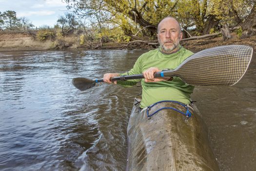 senior male paddler training in a fast sea kayak used in adventure racing, fall scenery, Poudre RIver in Fort Collins, Colorado, bow view