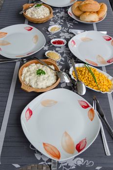 Finished table with red and white plates, cutlery and small dishes with side dishes to the barbecue.