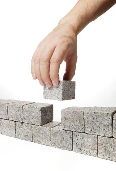 Man building a wall made of small blocks of granite rock.