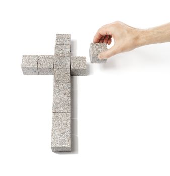 Man building a christian cross made of small blocks of granite rock.