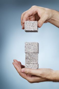 Man building a stack of granite rock blocks in his hands.