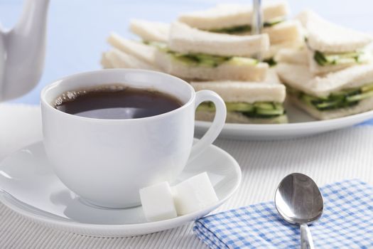 Cup of tea with cucumber sandwiches in background