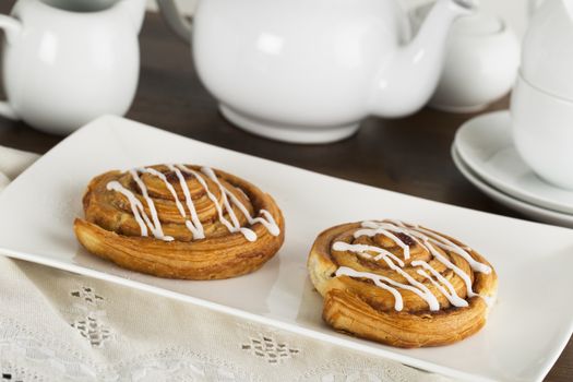 Two tempting cinnamon rolls with tea pot in background