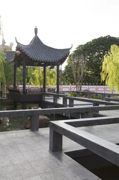 Chinese style pavilion on the pond with in park with ornamental trees.