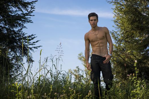 Gorgeous Young Shirtless Man with Sexy Abs, Strike a Pose at the Garden While Looking at the Camera.