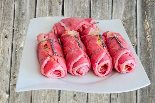 Non-fried beef rolls on white plate in wooden boards background
