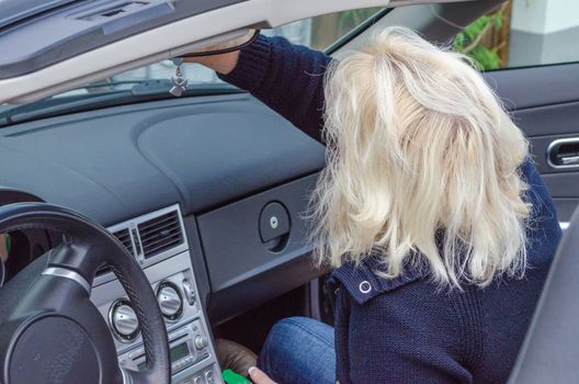 Woman with blond hair cleans the windshield of a convertible.
