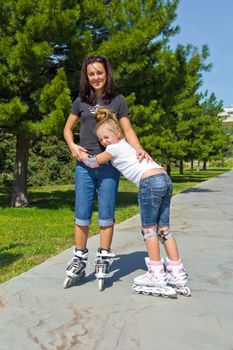 Learning mother and daughter on roller skates in summer