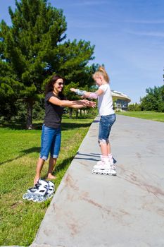 Learning mother and daughter on roller skates in summer