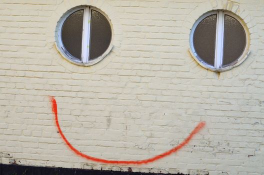 A smile in the spring. Graffiti face on a wall. 
With little effort by a line between two windows a smile brought to the wall. 
Despite smearing it prepares a smile.