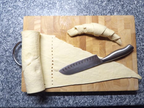 Raw croissant on a wooden board with a sharp knife
