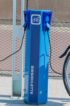 The Hague, Scheveningen Pier, Netherlands - August 7, 2014: Here in the photo the beach promenade of Scheveningen. There are charging point for electric bicycles. 
The picture shows an E-Bike which is connected for charging via cable to the station. Here e-bikes are available for rent.