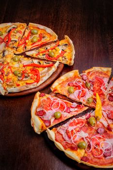 Two different pizzas with tomato, peppeeoni, olives, corn, red pepper