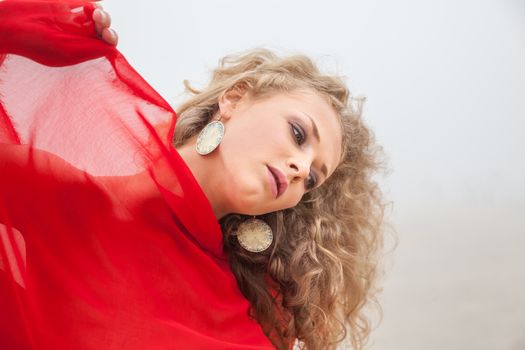 Beautiful woman in red fabric posing on sea beach in foggy day