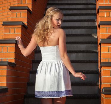 Coquettish young beautiful woman posing near the stairs at sunset