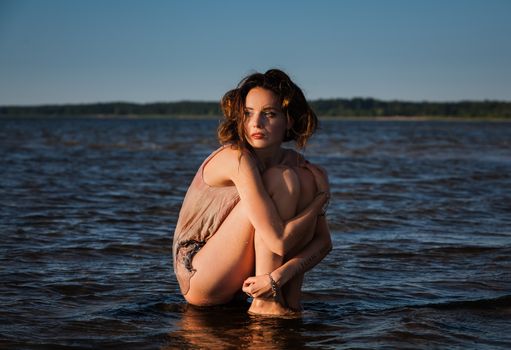 Attractive young seminude woman in a wet suit posing against the sea background