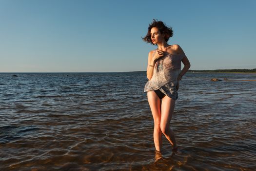 Attractive young seminude woman in a wet suit posing against the sea background