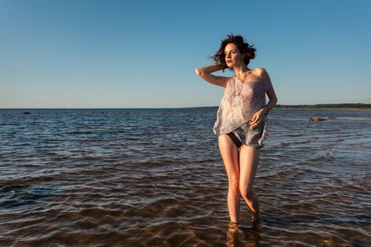 Attractive young seminude woman in a wet suit posing against the sea background