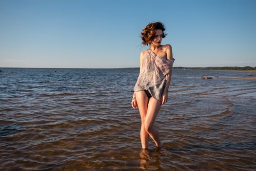 Attractive young seminude woman in a wet suit posing against the sea background