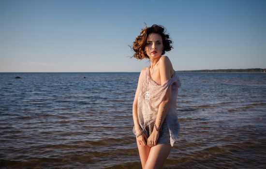 Attractive young seminude woman in a wet suit posing against the sea background