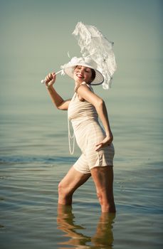 Woman in a striped retro bathing suit with a white parasol against the sea