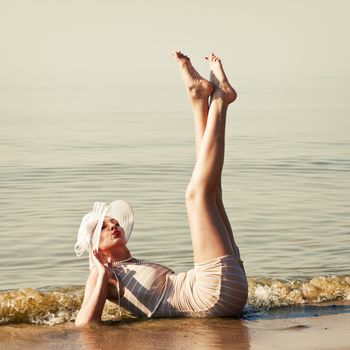 Coquettish woman in retro swimsuit lying in the water at the beach feet up