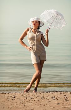 Woman in a striped retro bathing suit with a white parasol against the sea