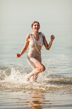 Woman in a striped retro bathing suit  runs along the water on the beach
